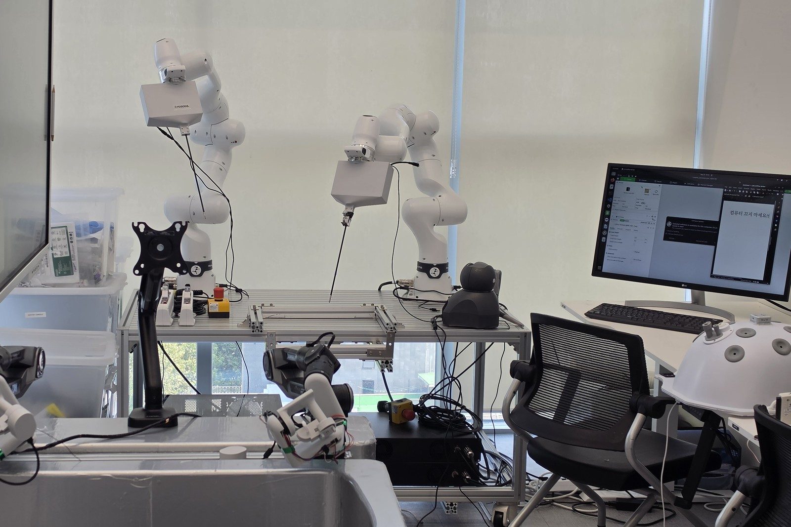 Laboratory with two Franka FR3 arms above a laparoscopic phantom and master console arms in the foreground